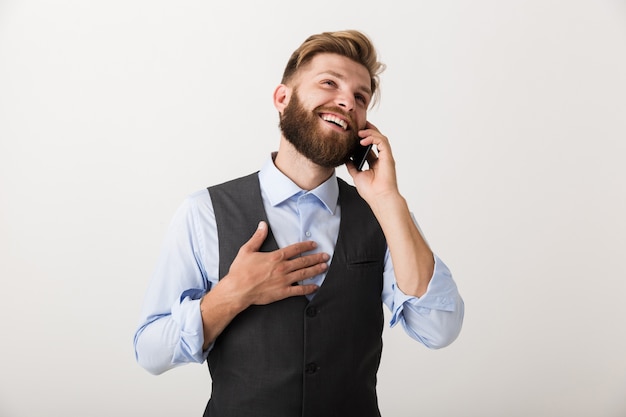 Obraz przystojny młody brodaty mężczyzna stojący na białym tle na tle białej ściany rozmawia przez telefon komórkowy.