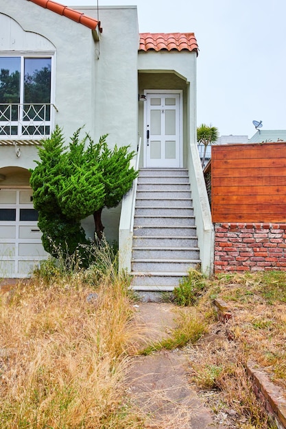 Obraz rozpadającego się chodnika obok zarośniętego trawnika ze schodami prowadzącymi do biało-szarych drzwi domu