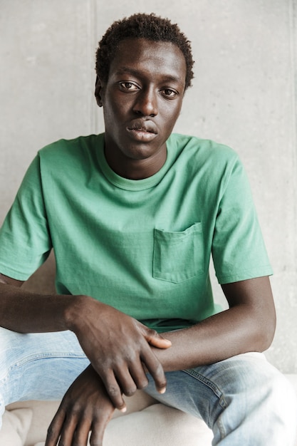 Obraz skoncentrowanego młodego Afroamerykanina w zwykłych ubraniach siedzącego nad ścianą w domu