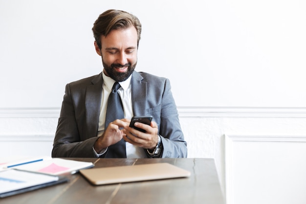 Obraz Uśmiechniętego Skoncentrowanego Biznesmena Noszącego Formalny Garnitur, Piszącego Na Telefonie Komórkowym Podczas Pracy W Biurze
