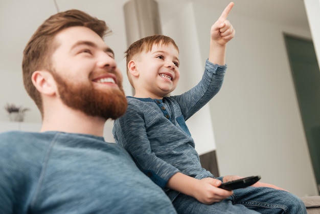 Obraz wesoły ojciec ogląda telewizję z jego małym ładnym synem trzymającym pilota.