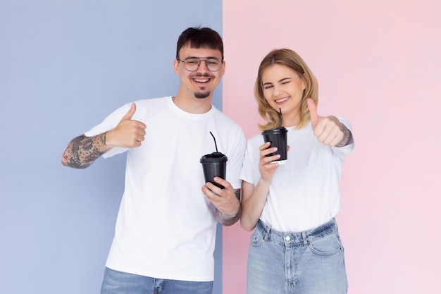 Obraz zadowolony para mężczyzna i kobieta w dżinsowych ubraniach uśmiechający się, trzymający filiżanki z kawą na wynos