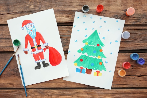 Obrazy dziecka przedstawiające choinkę z prezentami i Mikołajem na stole
