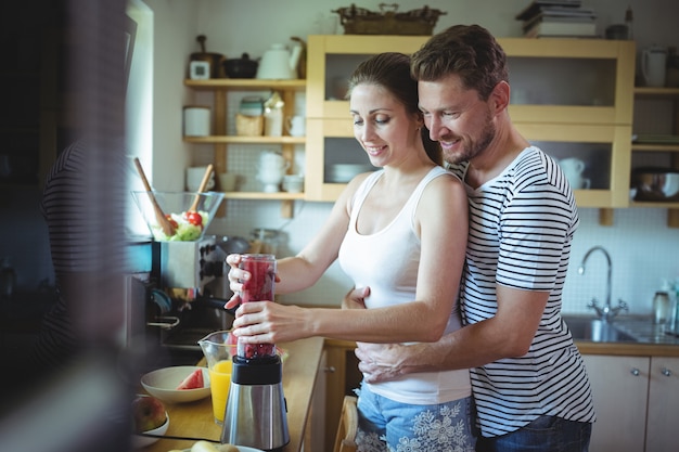 Obsługuje Obejmowanie Kobiety Od Behind Podczas Gdy Przygotowywający Arbuza Smoothie W Kuchni