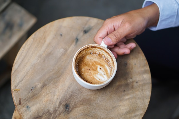 Obsługuje rękę trzyma Latte sztuki filiżankę na drewnianym stole