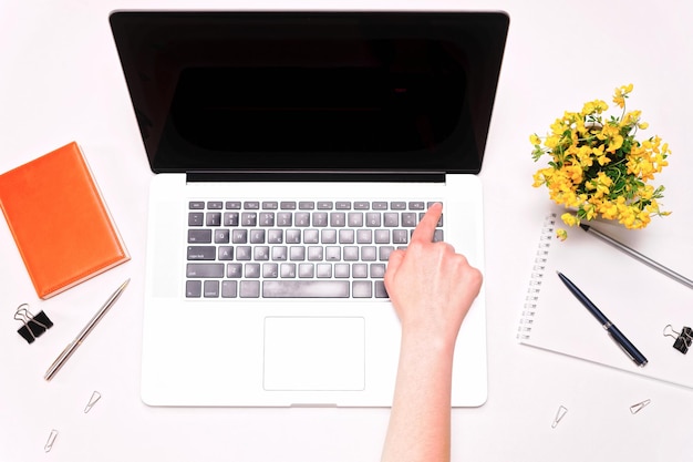 Obszar roboczy i ręka kobieta pracuje na klawiaturze laptopa i żółte kwiaty na białym tle. Płaski układanie, widok z góry