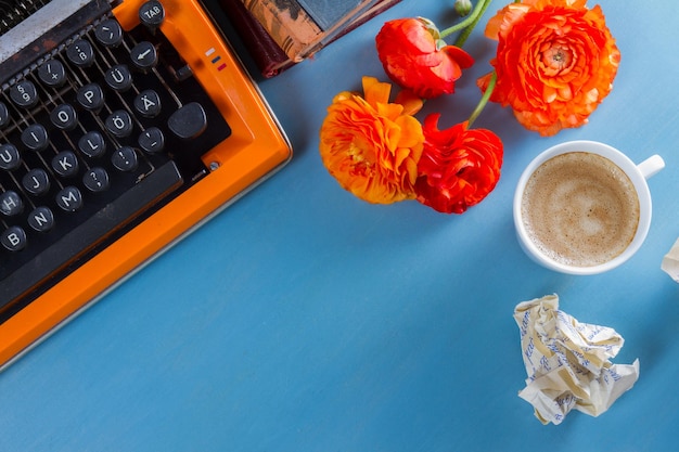 Obszar Roboczy Z Pomarańczową Maszyną Do Pisania W Stylu Vintage Z Kwiatami I Kawą, Skopiuj Miejsce Na Niebieskim Tle Stołu