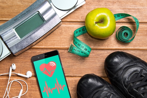 Obuwie sportowe, jabłko, waga i telefon z kartą zdrowia na drewnianym stole