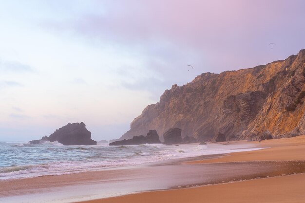 Ocean dzikiej plaży sztormowa pogoda Praia da Adraga piaszczysta plaża z malowniczym krajobrazem w tle Sintra Cascais Portugalia