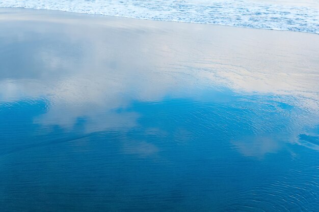 Oceaniczna plaża z powracającą falą, w której odbija się niebo