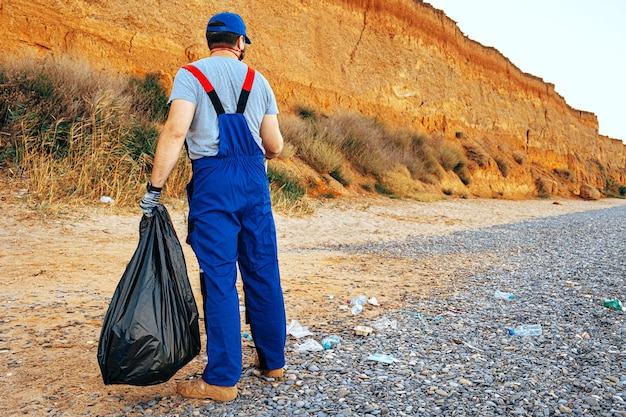 Ochotnik stojący na plaży z pełną torbą zebranych śmieci