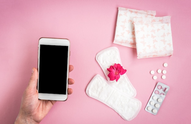 Ochrona higieny kobiety. Podpaski z tabletką przeciwbólową, różową różą i różowym telefonem komórkowym.