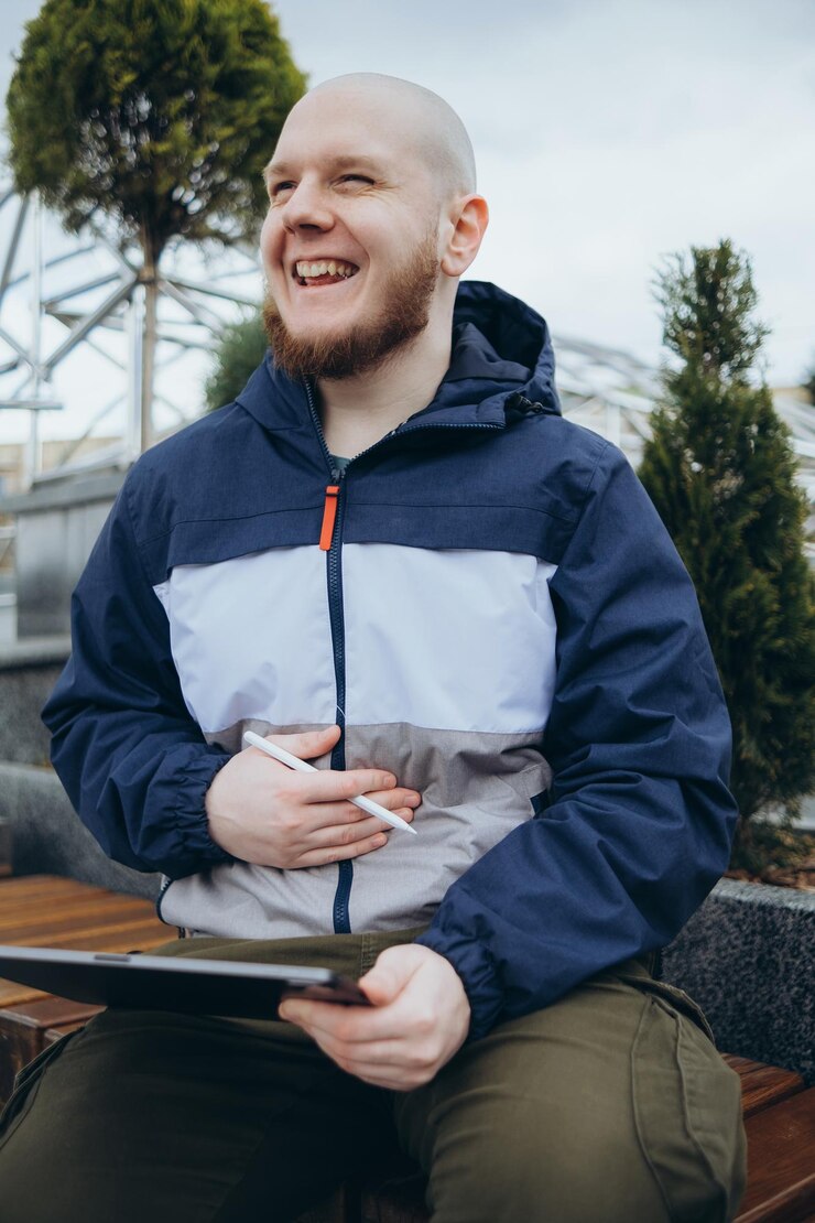 Zdjęcie od dołu hipstera używającego nowoczesnego tabletu z rysikiem podczas tworzenia nowego projektu i siedzącego na ulicy