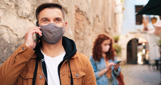 Zdjęcie od pasa w górę portret brunetki kaukaskiego mężczyzny noszącego ochronną maskę na twarz rozmawiający...