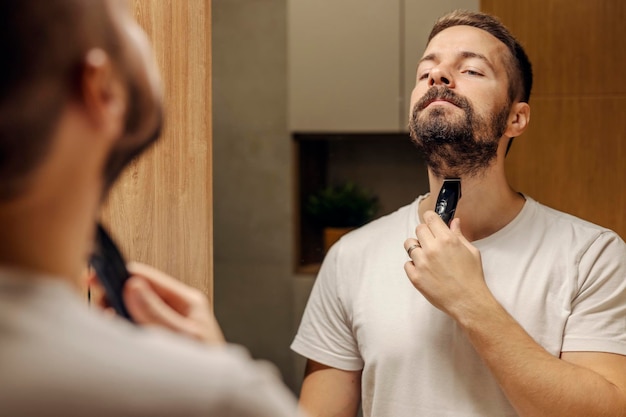 Odbicie mężczyzny przycinającego brodę w łazience przed lustrem
