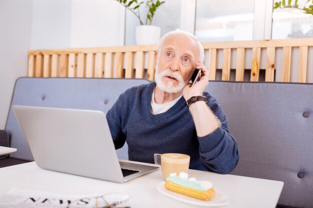 Odblaskowy starszy freelancer za pomocą laptopa i rozmawia przez telefon