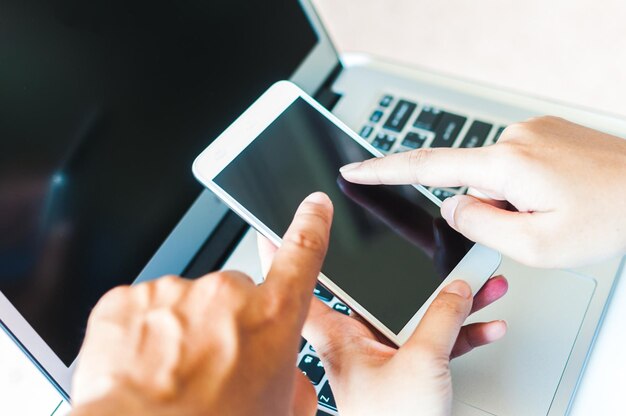 Odcięta ręka bizneswoman i koleżanki używającej telefonu komórkowego i laptopa na stole