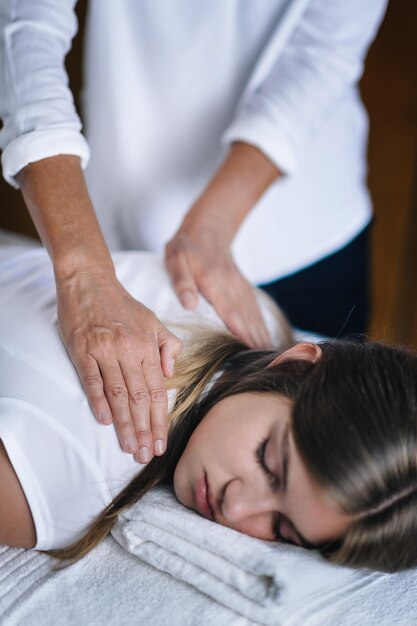 Zdjęcie odcięte ręce terapeutki podającej leczenie reiki nastolatce na twarzy w spa