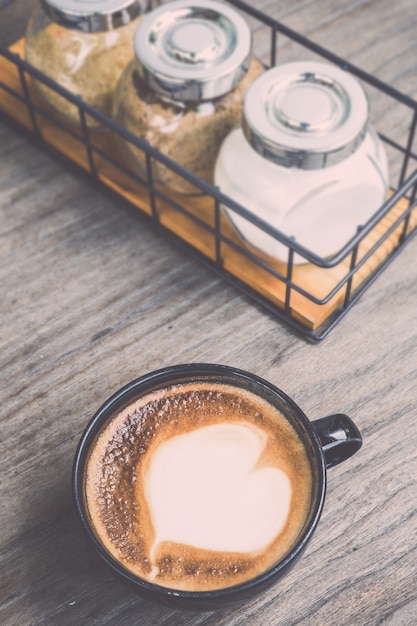 Odgórnego widoku gorąca latte kawa w czarnej filiżance na popielatym drewnianym stołowym tle. Vintage efekt filtra