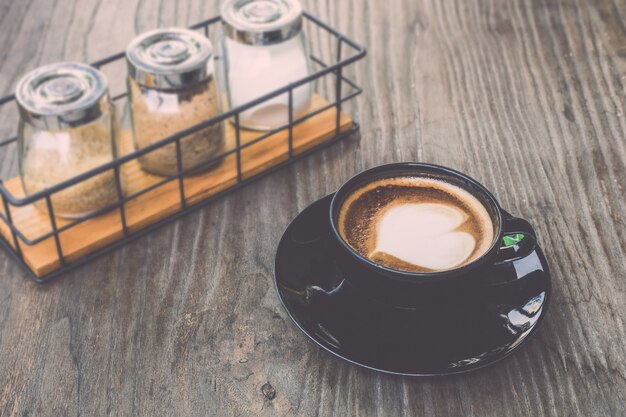 Odgórnego widoku gorąca latte kawa w czarnej filiżance na popielatym drewnianym stołowym tle. Vintage efekt filtra