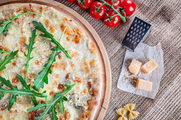 Zdjęcie odgórnego widoku pizzy cztery ser z arugula na drewnianym tle. kuchnia włoska. przekąska i fast food. zdjęcie żywności w poziomie. pizza z dodatkami na stole. wyśmienicie pizza z kopii przestrzenią
