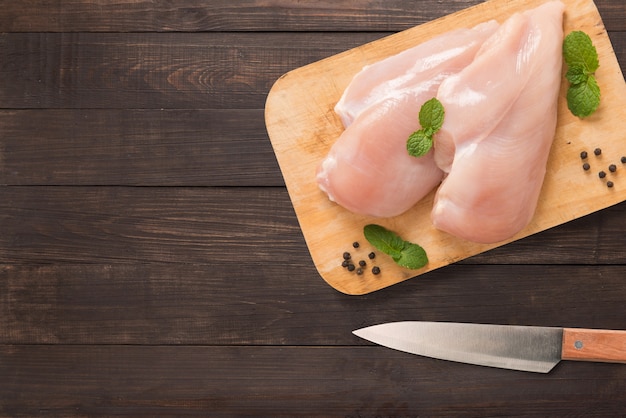 Odgórnego widoku surowy kurczak na tnącej desce i nóż na drewnianym tle. Copyspace dla tekstu