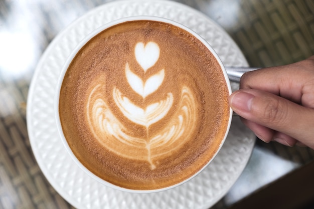 Odgórnego Widoku Wizerunek Trzyma Filiżankę Gorąca Latte Kawa Z Latte Sztuką Na Stole Ręka