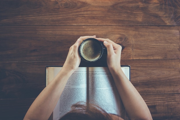 Odgórny widok czyta książkę i trzyma filiżankę kawy młoda kobieta