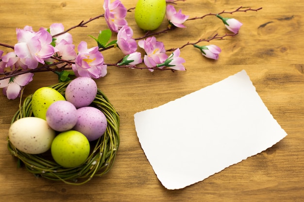 Zdjęcie odgórny widok kolorowi wielkanocni jajka w wierzby gniazduje, wiosna kwitnie i wiadomości karta na brown drewnianym tle.