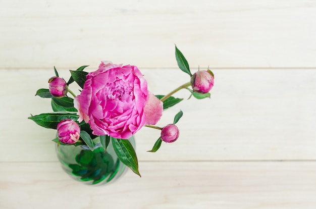 Zdjęcie odgórny widok kwitnąć piękną świeżą różową peonię i pączki w wazie na lekkim drewnianym tle
