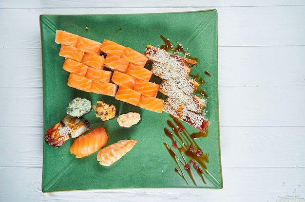 Odgórny widok na secie asortowana rolka i suszi na zieleń talerzu odizolowywającym na białym drewnianym tle. Sushi z łososiem, węgorzem. japońskie sushi