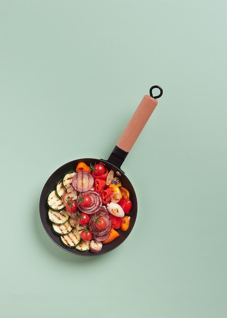 Odmiana grillowanych warzyw na żeliwnej patelni z drewnianym uchwytem, widok z góry: cukinia, czerwona cebula; czerwona, pomarańczowa i żółta papryka, bakłażan i pomidorki koktajlowe