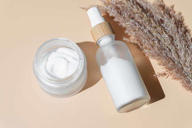 Odmładzające kolagenowe serum do twarzy w szklanej butelce i kremie do twarzy na beżowym tle z miejscem na kopię Natural Organic Cosmetic Beauty Concept