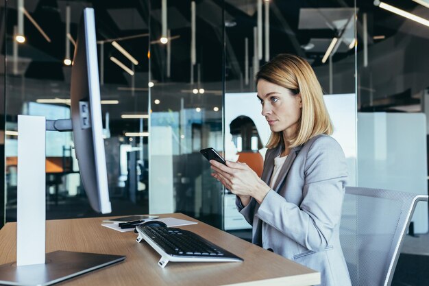 Odnosząca sukcesy kobieta pracująca w nowoczesnym biurze na komputerze bizneswoman korzysta z telefonu w sieciach społecznościowych, przeglądając internet