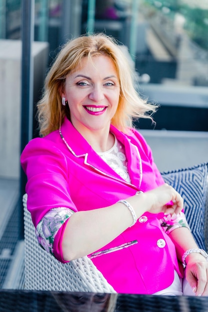 Odnosząca sukcesy kobieta przedsiębiorca w purpurowej kurtce pozuje na tarasie kawiarni w centrum biznesowym