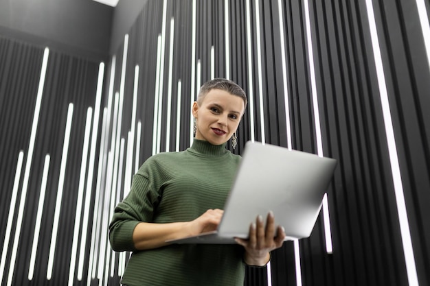 Odnosząca sukcesy programistka z laptopem w dłoniach z krótką fryzurą na szarej ścianie