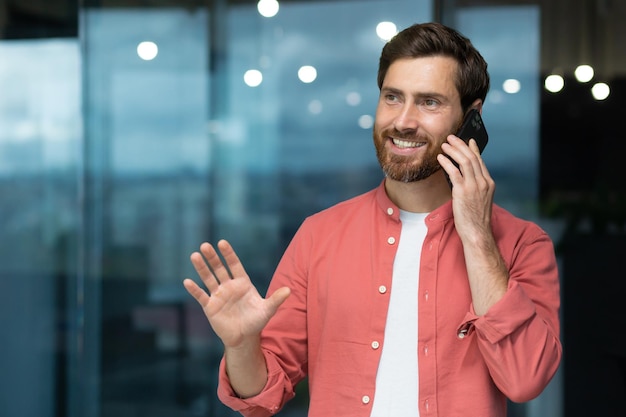 Odnoszący sukcesy biznesmen w czerwonej koszuli rozmawiający przez telefon w biurze mężczyzny z brodą