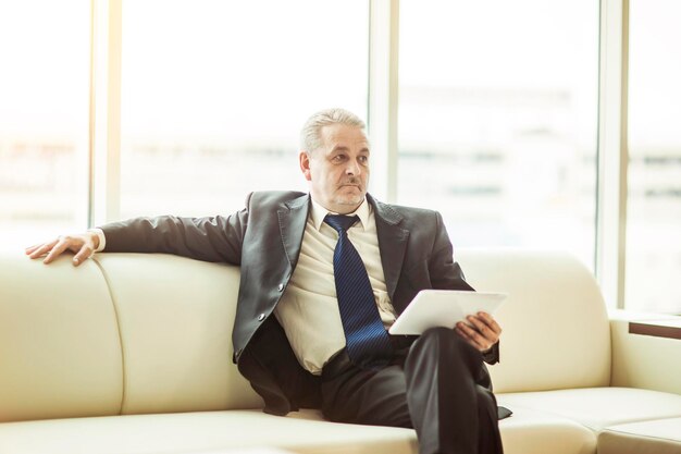 Odnoszący sukcesy biznesmen z cyfrowym tabletem siedzącym na kanapie w biurze