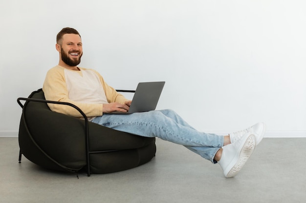 Odnoszący sukcesy freelancer, korzystający z laptopa siedzącego na krześle w pomieszczeniu