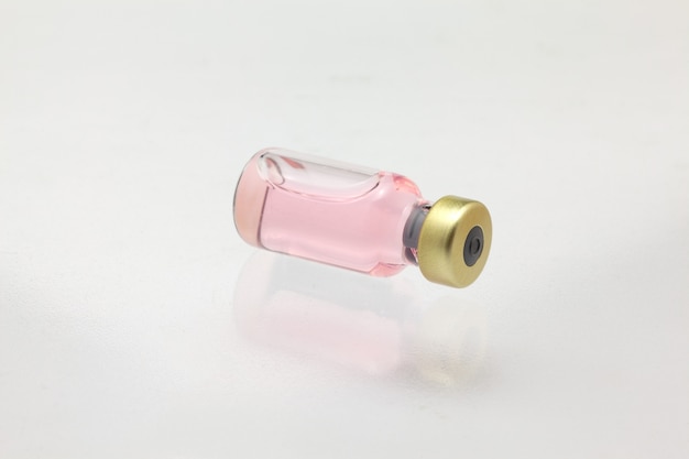 Odosobniona szklana butelka szczepionki leżąca z kolorowym płynem bardzo blisko makiety dużego powiększenia