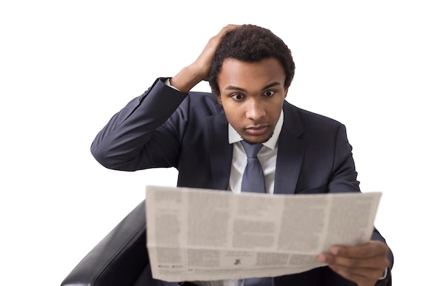 Zdjęcie odosobniony portret zaskoczonego afroamerykanina biznesmena siedzącego w fotelu z gazetą i patrzącego na to z niedowierzaniem