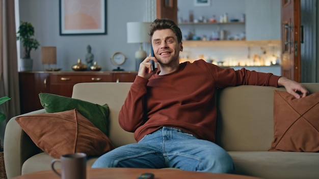 Odpoczywający facet komunikuje się smartfonem na przytulnej kanapie szczęśliwy człowiek rozmawia przez telefon komórkowy