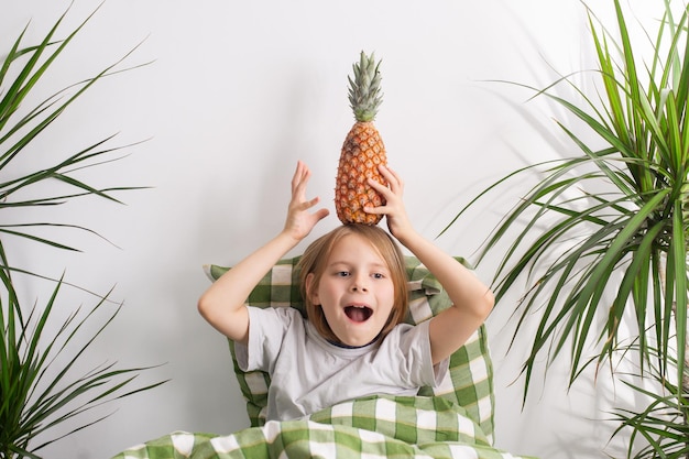 Odpoczywający w łóżku 910-letni chłopiec z długimi włosami oddaje się bezczynności, trzymając w rękach ananas.