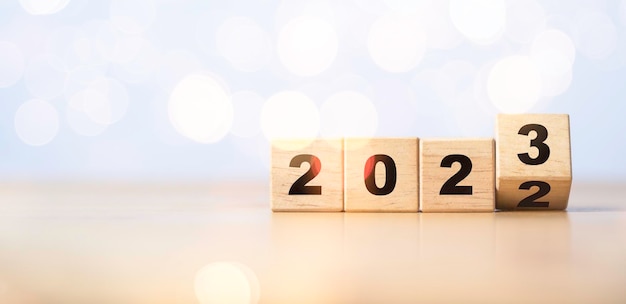 Odwracanie drewnianej kostki blokowej, aby zmienić 2022 na 2023 z bokeh na wesołe święta i koncepcję przygotowania szczęśliwego nowego roku