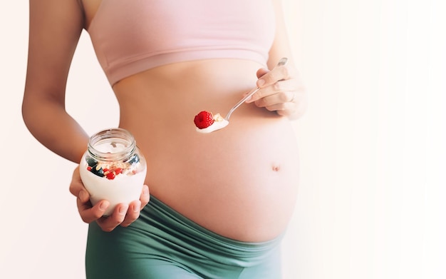 Odżywianie i dobre samopoczucie podczas ciąży Zbliżenie brzuch w ciąży ze zdrową przekąską jogurt z muesli i jagodami Koncepcja wyboru styl życia dieta sport zdrowe ciało kobiety w ciąży