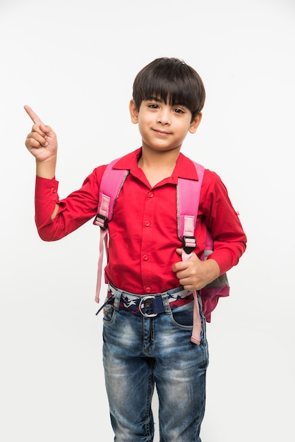 Off to School - Śliczny mały indyjski lub azjatycki chłopiec w czerwonej koszuli i dżinsach z tornisterem, stojący na białym tle nad białym tłem