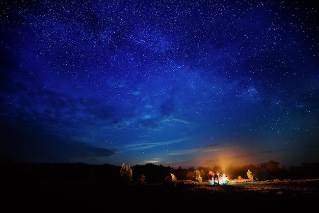 Ognisko kempingowe pod niesamowitym błękitnym rozgwieżdżonym niebem z mnóstwem świecących gwiazd i chmur Podróżuj rekreacyjną koncepcją aktywności na świeżym powietrzu