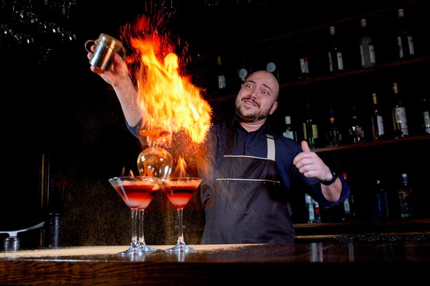 Ognisty pokaz w barze. Barman robi gorący koktajl alkoholowy i rozpala bar. Barman przygotowuje ognisty koktajl. Ogień na barze.