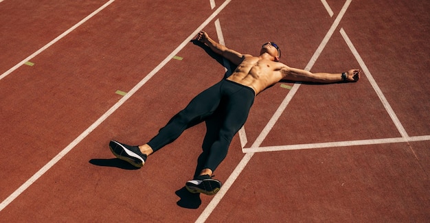 Ogólny widok obrazu młody przystojny lekkoatletka shirtless mężczyzny leżącego na torze wyścigowym na stadionie, odpoczywając Profesjonalny sportowiec odpoczywa po sesji treningowej Ludzie sport i zdrowy styl życia