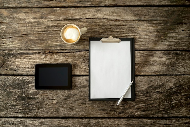 Ogólny widok teksturowanego rustykalnego drewnianego gabinetu lub biurka z pustą białą kartką papieru cyfrowego tabletu i filiżanką świeżej kawy